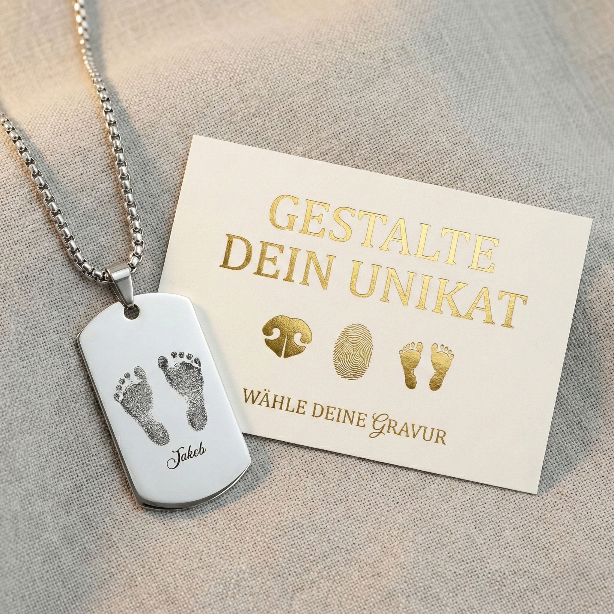 gravierter anhänger mit babyfüßen auf naturfarbenem leinen mit einer KArte zum gestalten des eigenen unikates
