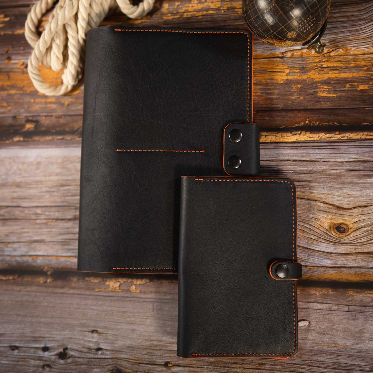 Handgefertigte schwarze Leder-Heimtierausweishülle mit orangefarbenen Kontrastnähten, stilvoll arrangiert neben einem passgenauen, sportlichen Travel Wallet