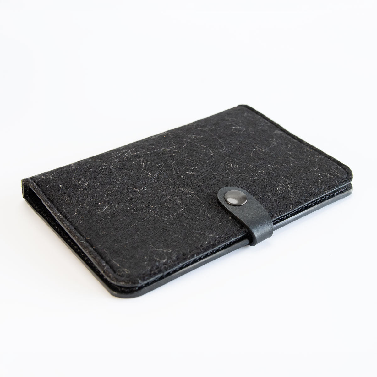Vorderseite der geschlossenen Heimtierausweishülle aus schwarzem Boxcalf-Leder und schwarz-meliertem Filz mit edlem Gunmetal-Druckknopf.