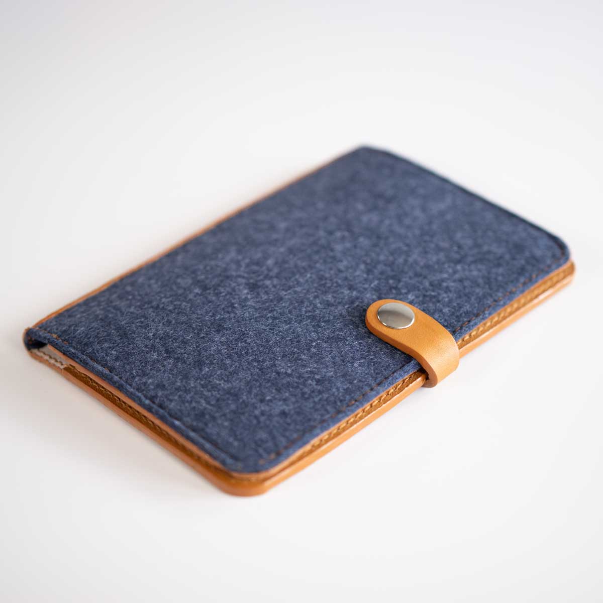Vorderseite der geschlossenen Kombi-Heimtierausweishülle aus dunkelblauem Denim-Filz und cognacfarbenem Leder mit silbernem Druckknopf.