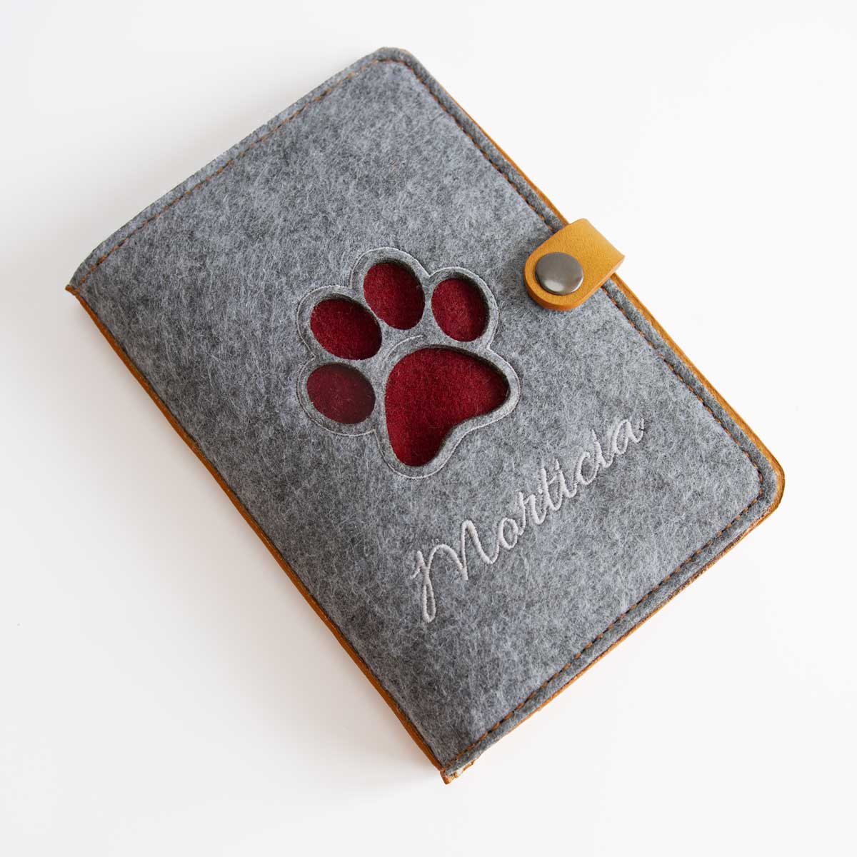 Geschlossene Heimtierausweishülle aus cognacfarbenem Leder und grauem Filz mit personalisiertem Namensstick und Pfoten-Lasercut.