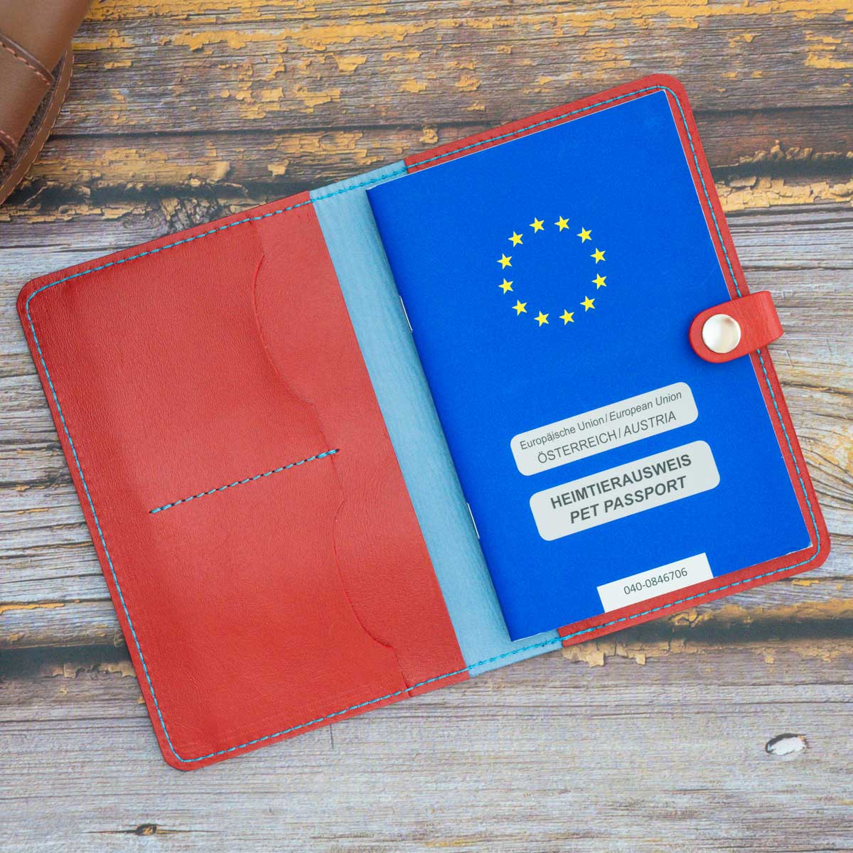 Geöffnete Leder-Impfpasshülle in Signalrot und Hellblau, befüllt mit einem blauen EU-Heimtierausweis und Sicht auf die praktische Fächeraufteilung.