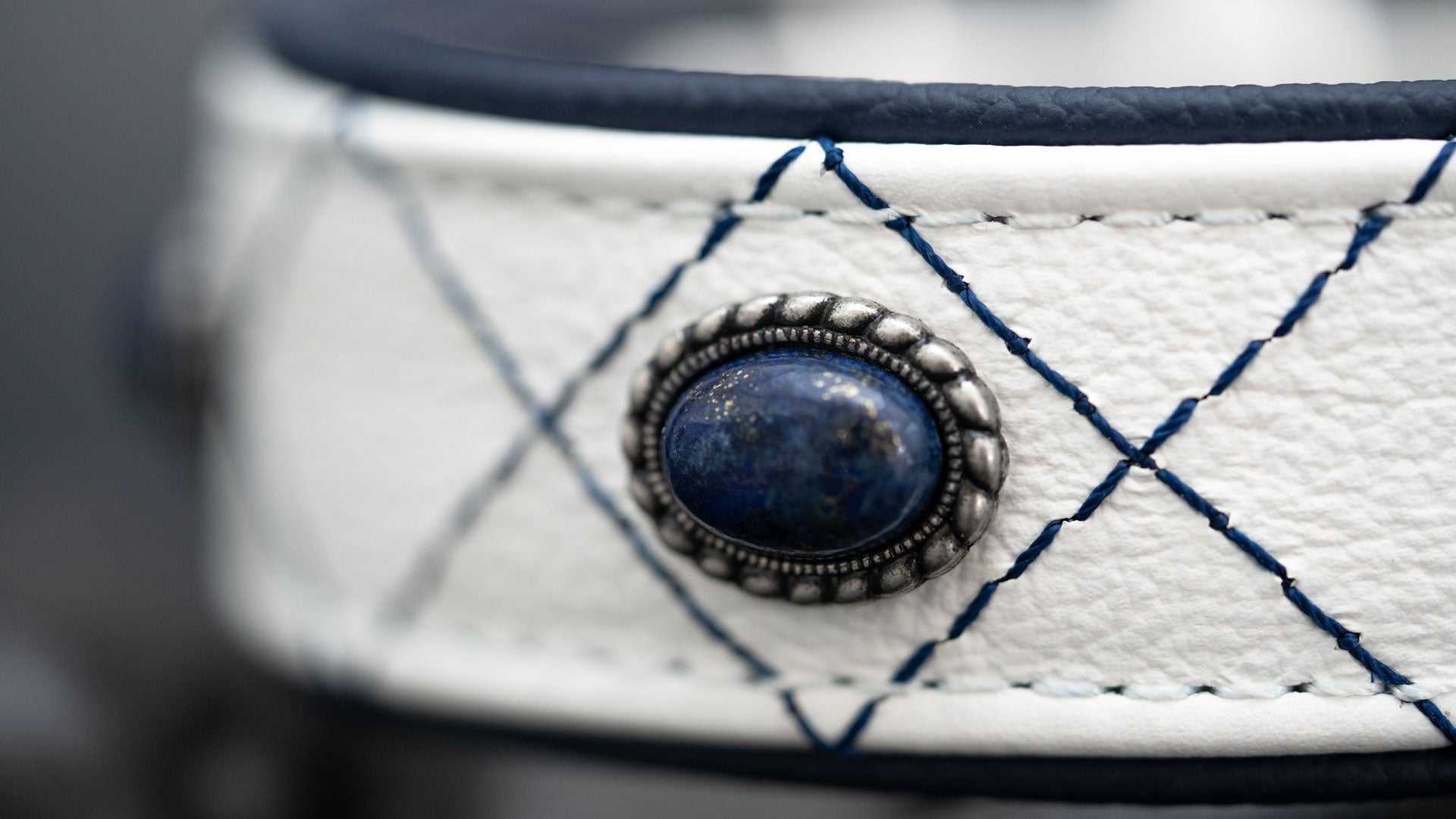 Detailansicht von Lapislazuli, Metallfassung und dunkelblauer Steppung auf weißem Nappaleder