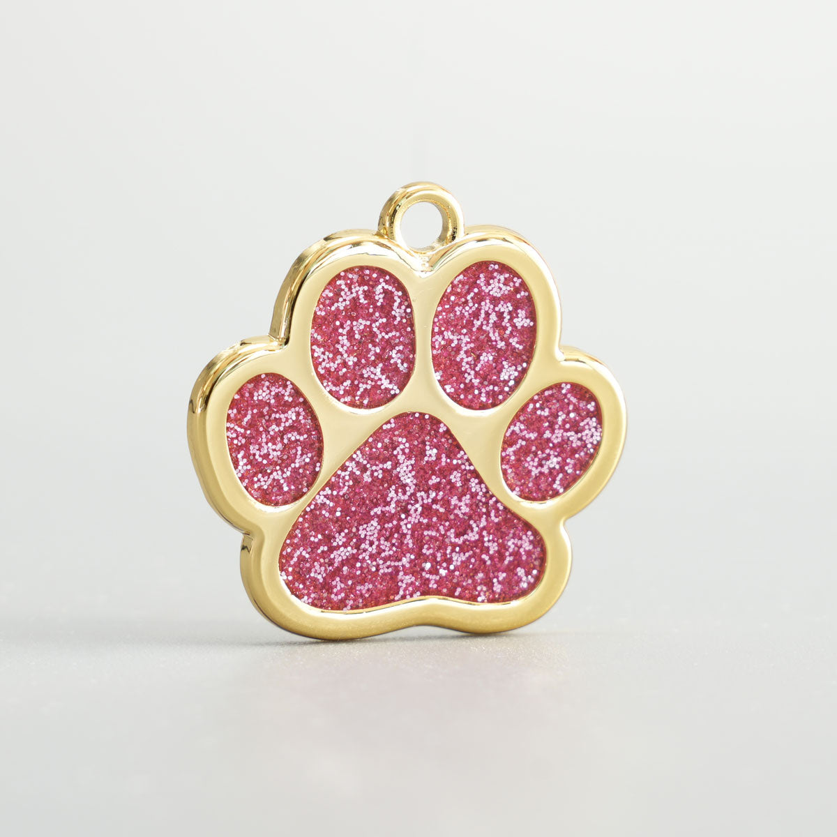 Nahaufnahme einer goldenen Hundemarke in Pfotenform mit rosa 
Glitzer-Epoxidharz und Aufhängung.