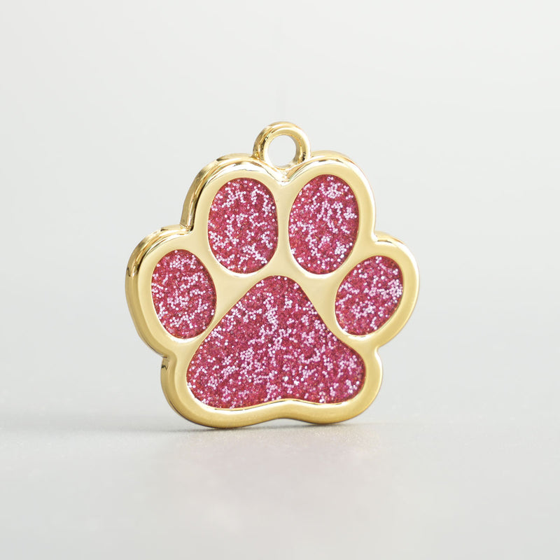 Nahaufnahme einer goldenen Hundemarke in Pfotenform mit rosa Glitzer-Epoxidharz und Aufhängung.