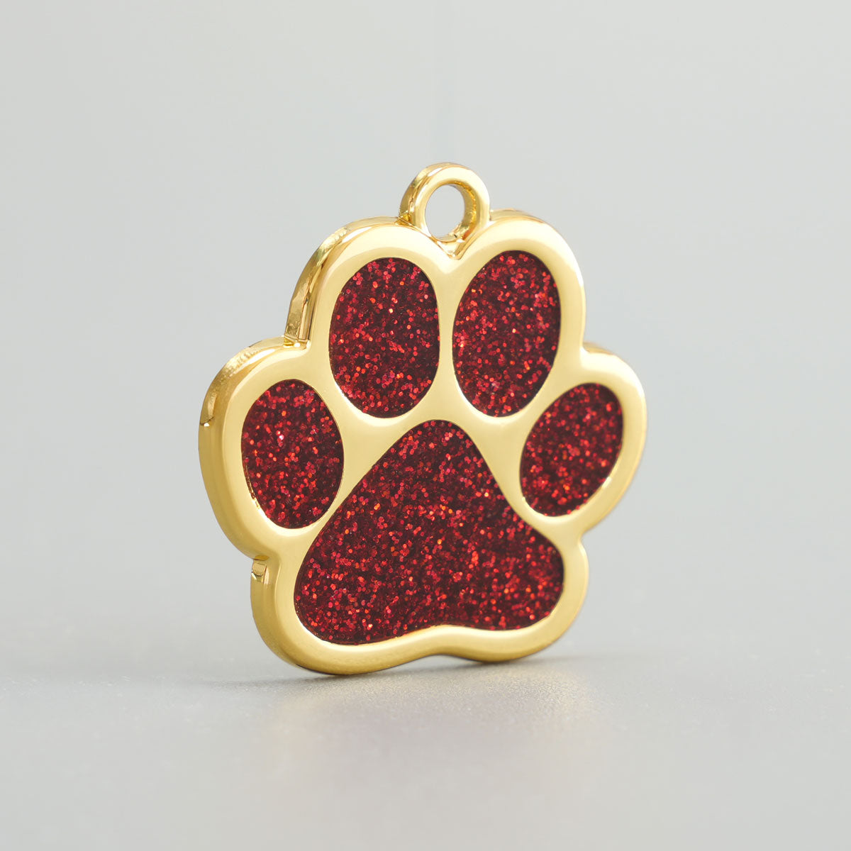 Nahaufnahme einer goldenen Hundemarke in Pfotenform mit rotem Glitzer-Epoxidharz und Aufhängung.