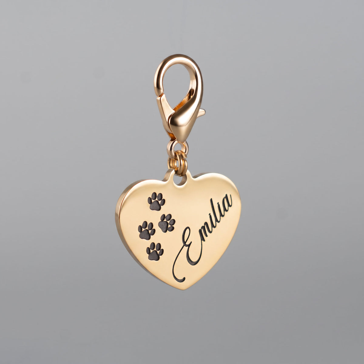 Goldfarbene Edelstahl-Hundemarke in Herzform mit tief graviertem Rufnamen Emilia, vier Pfotenmotiven und Karabiner.