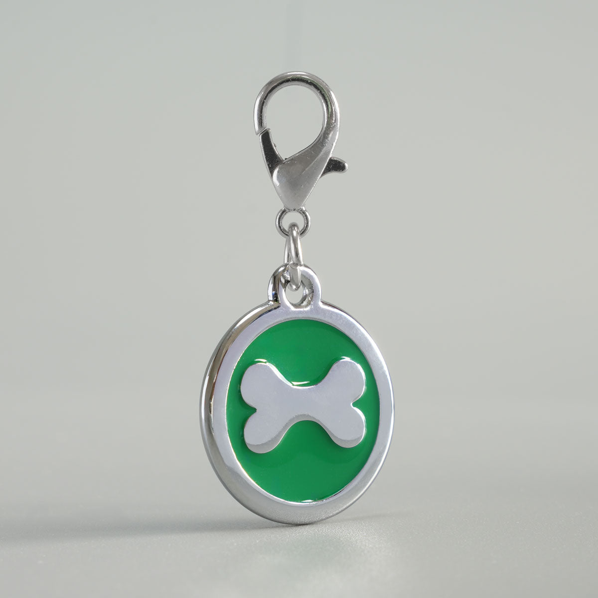 Detailansicht einer grünen, runden Hundemarke aus verchromtem Druckguss mit silbernem Knochen-Inlay und Karabiner
