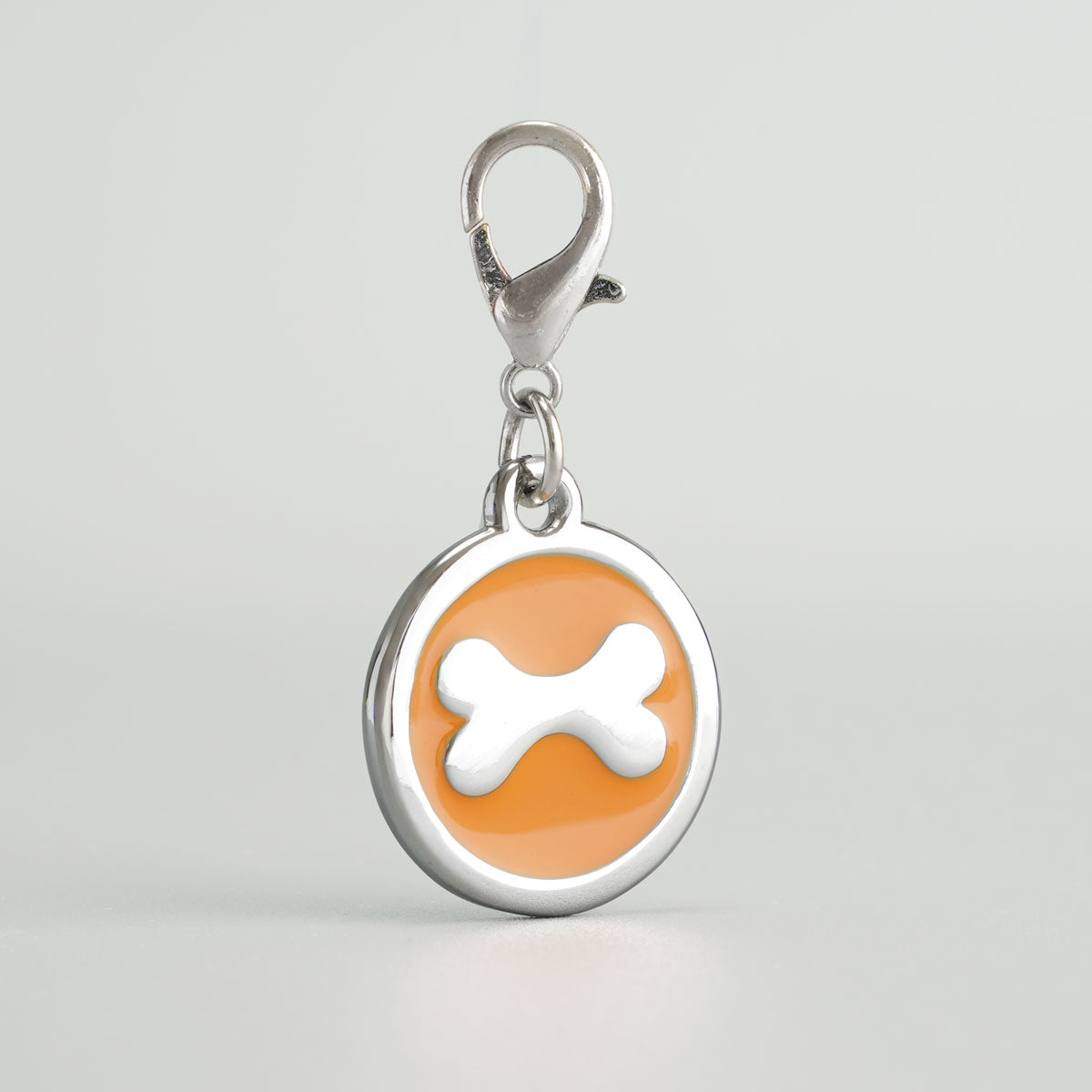 Detailansicht einer orangen, runden Hundemarke aus verchromtem Druckguss mit silbernem Knochen-Inlay und Karabiner