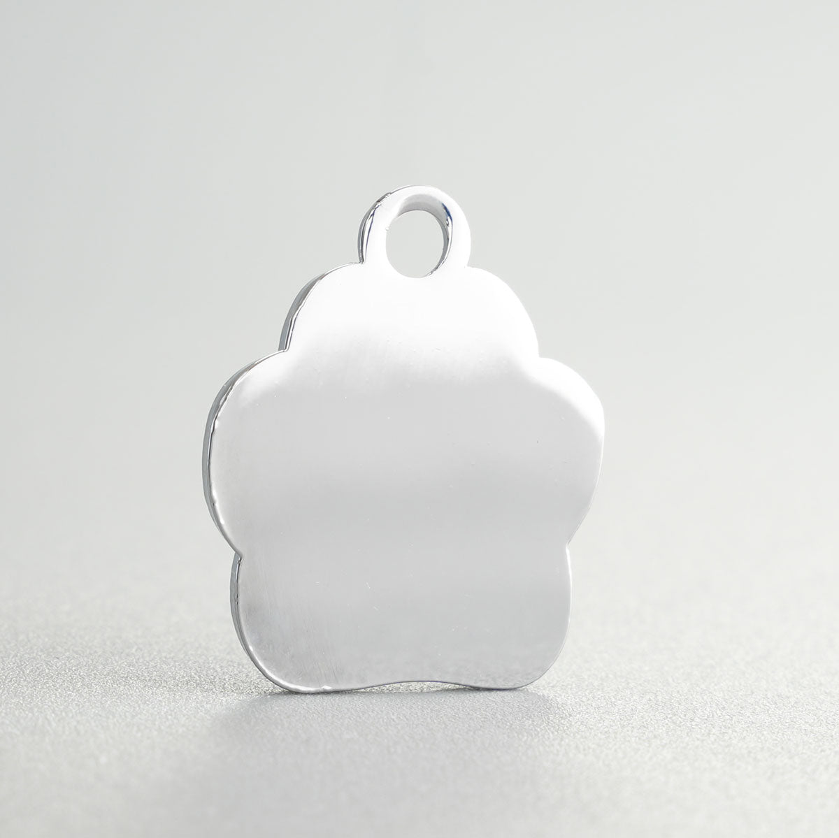 Nahaufnahme einer verchromten Hundemarke in Pfotenform Rückansicht vor der Gravur