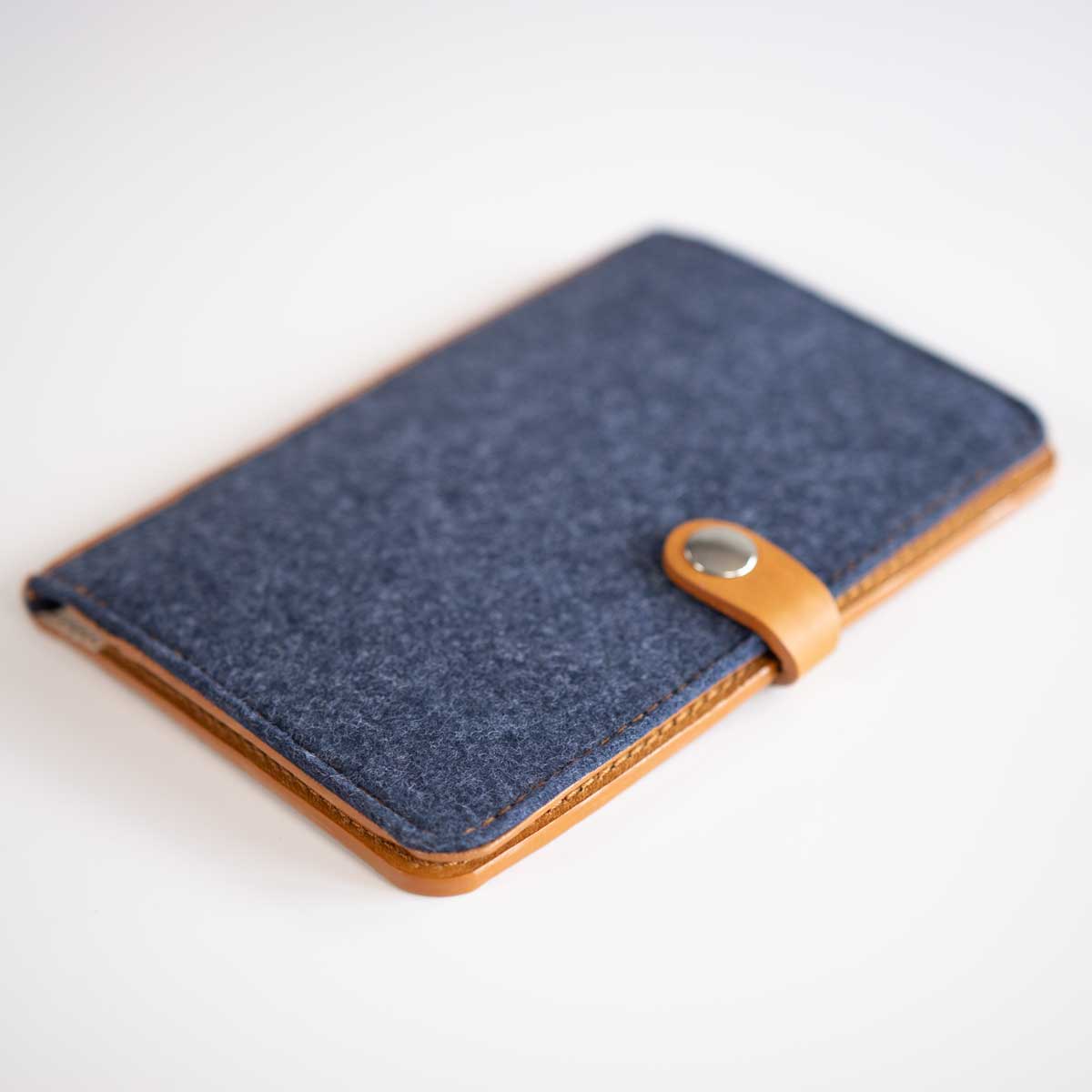 Schräge Ansicht der handgefertigten Leder-Filz-Hülle, die die harmonische Materialkombination aus Cognac und Denim-Blau zeigt.