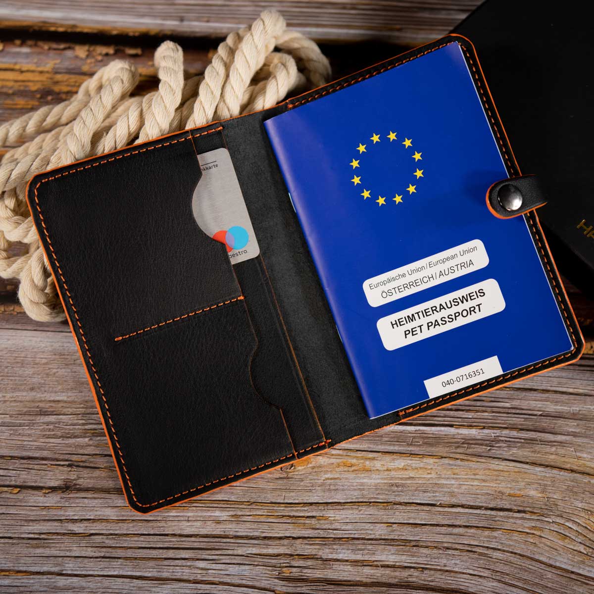 Innenansicht der schwarzen Lederhülle mit orangefarbenen Kanten, befüllt mit einem EU-Heimtierausweis und vielseitigen Einschubfächern für Karten