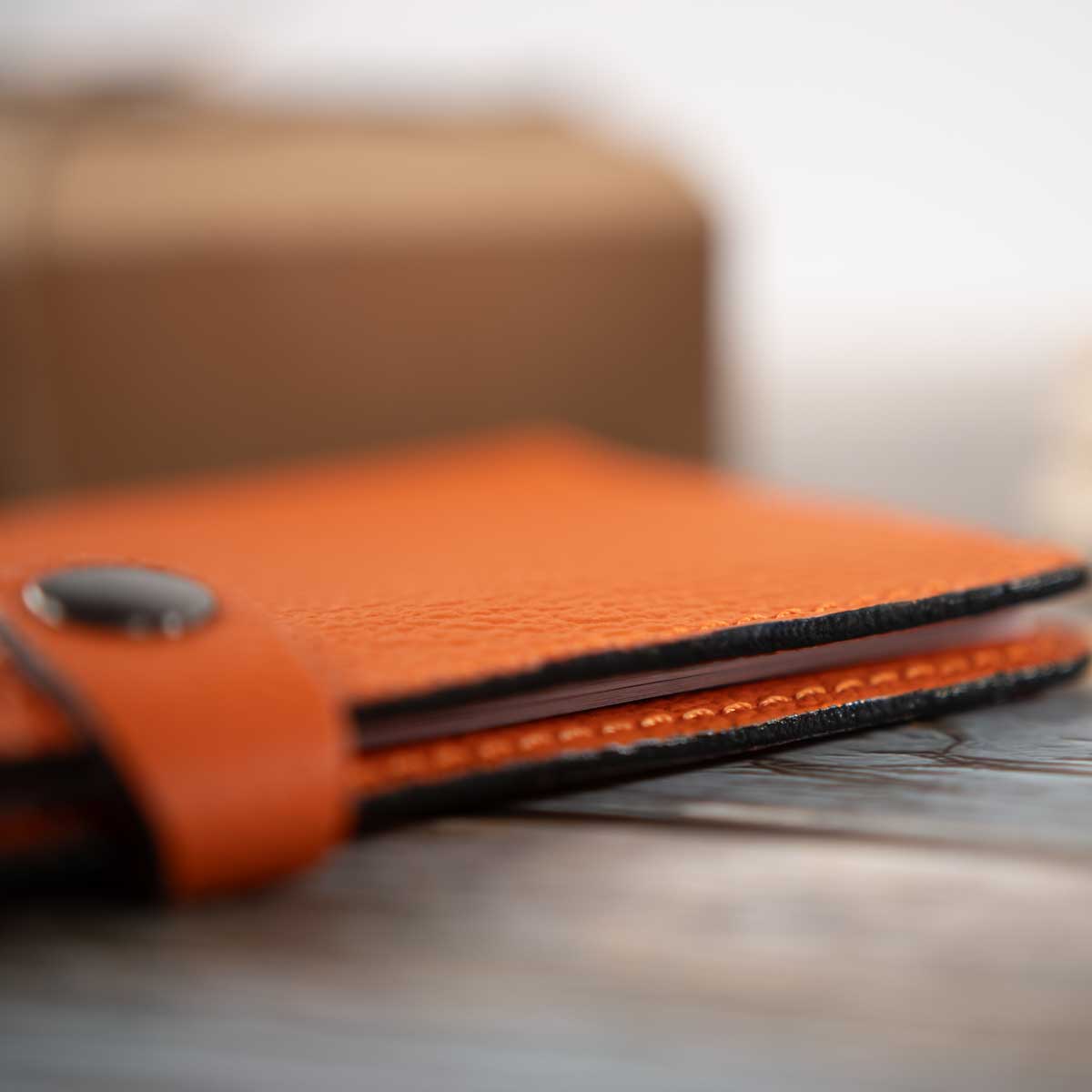 Nahaufnahme der handwerklich präzise geschliffenen, schwarz lackierten, versiegelten und auf Hochglanz polierten Lederkanten der orangen Hülle.