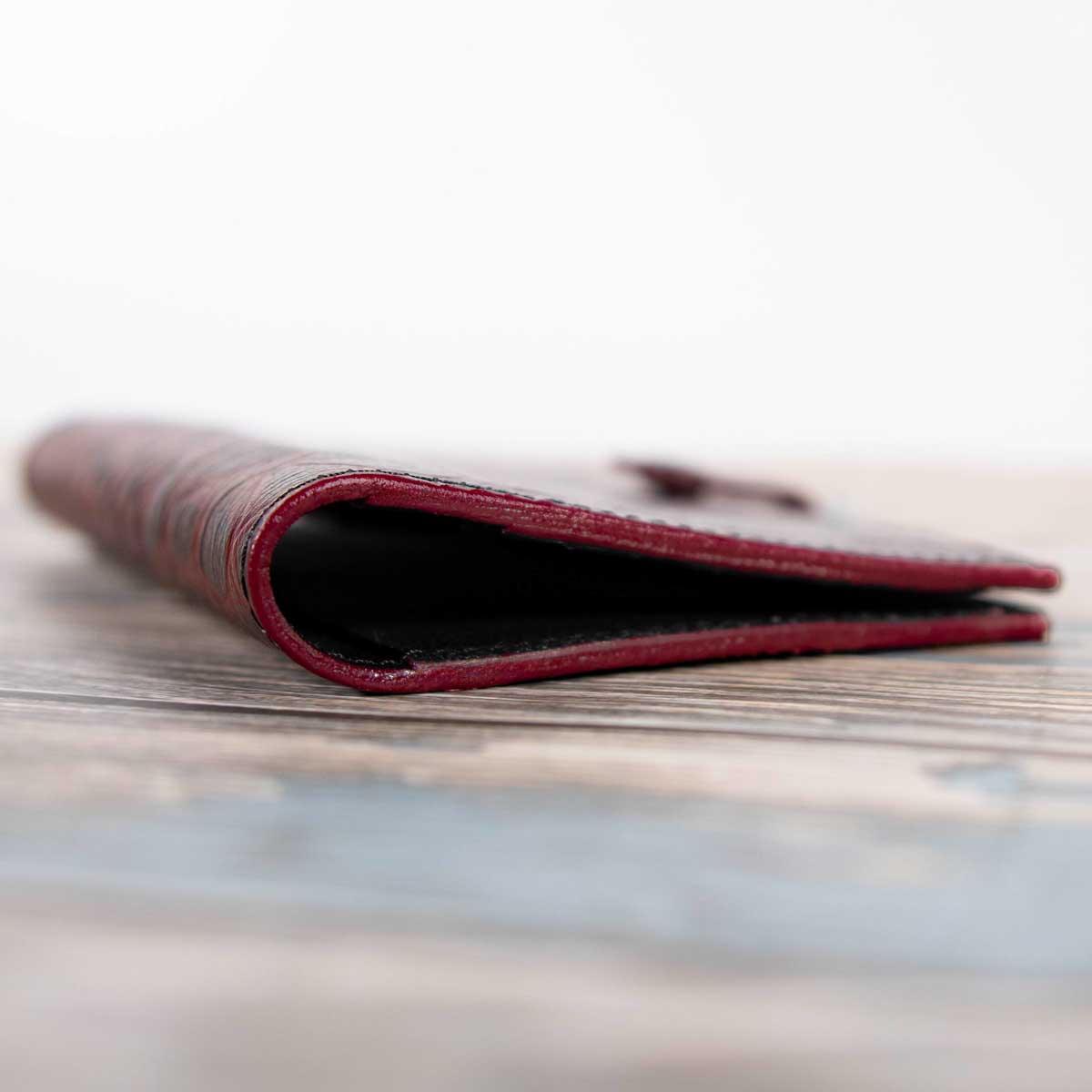 Nahaufnahme der professionell in Handarbeit geschliffenen, lackierten, versiegelten und auf Hochglanz polierten Lederkanten des rot-schwarzen Travel Wallets.