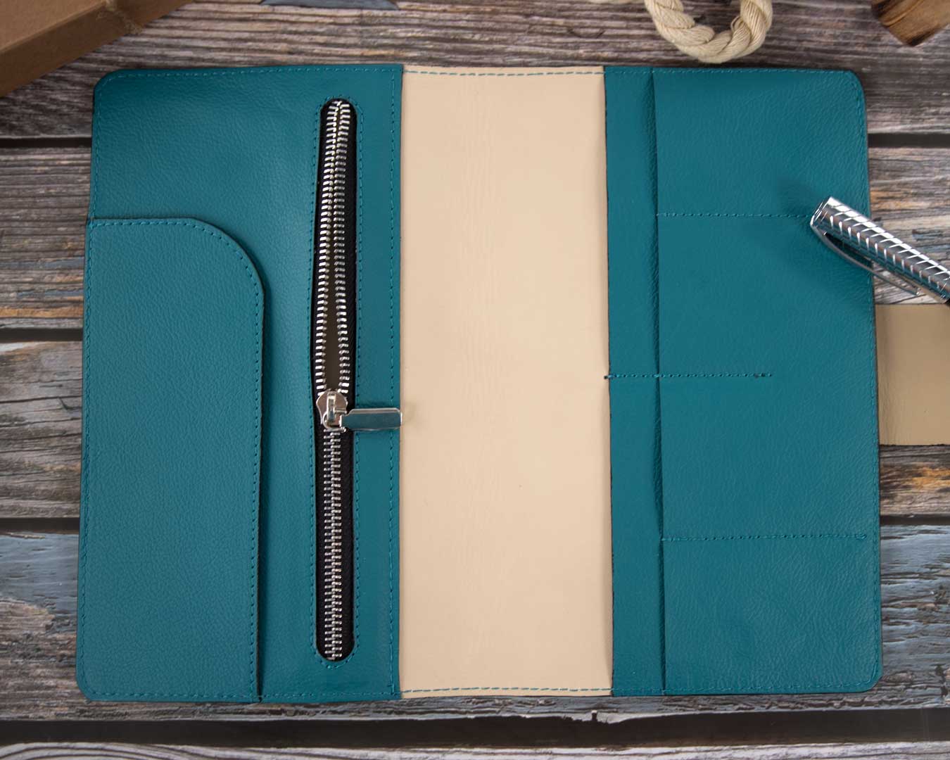 Elegantes petrolfarbenes Travel Wallet aus italienischem Taschenleder, liegend neben einem Paket auf einem Holztisch