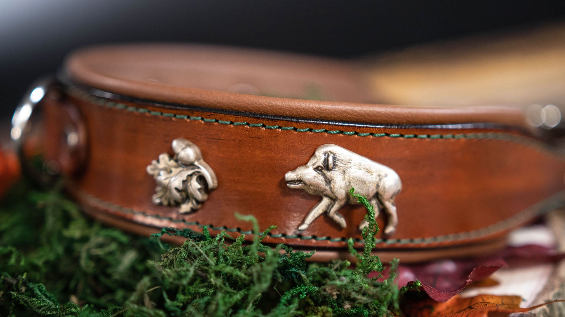 detailansicht des handgefertigten lederhlasband. zu sehen ist ein wildschwein und eichenlaub