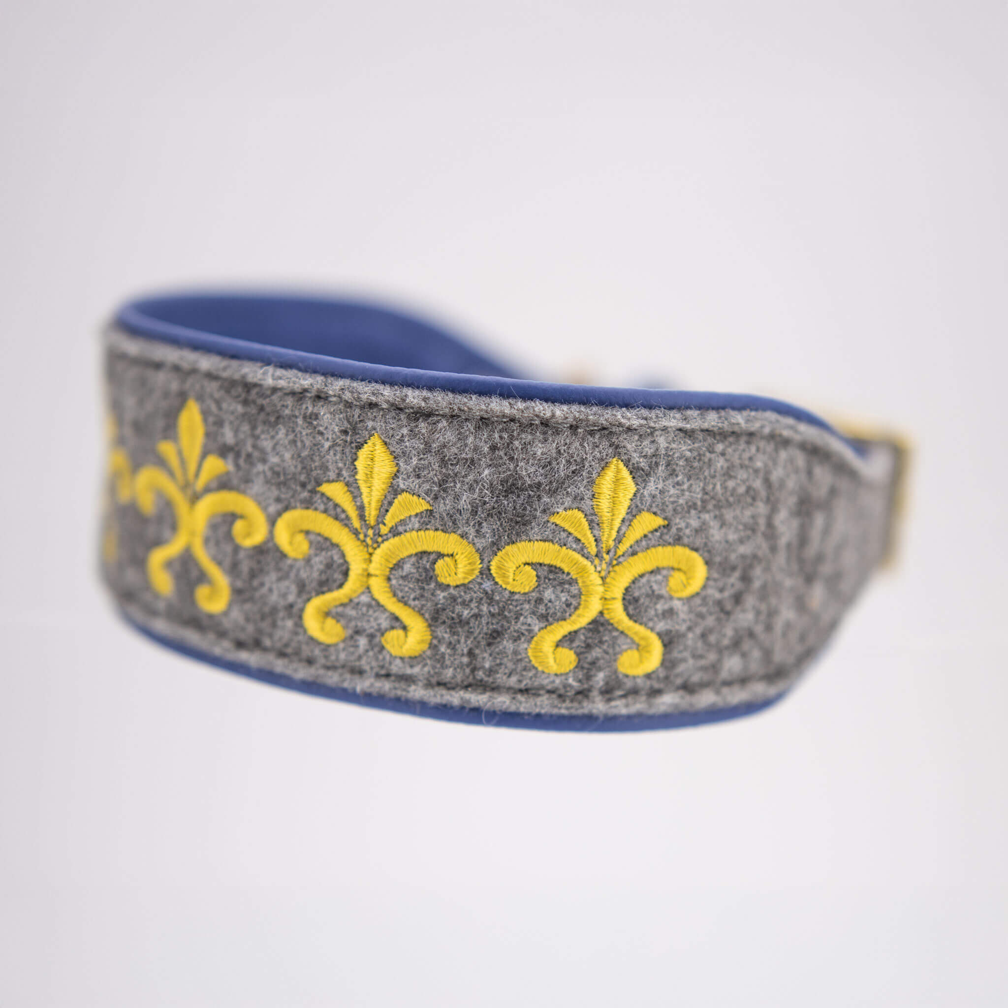 Detailaufnahme der goldenen Lilien-Stickerei auf grauem Wollfilz