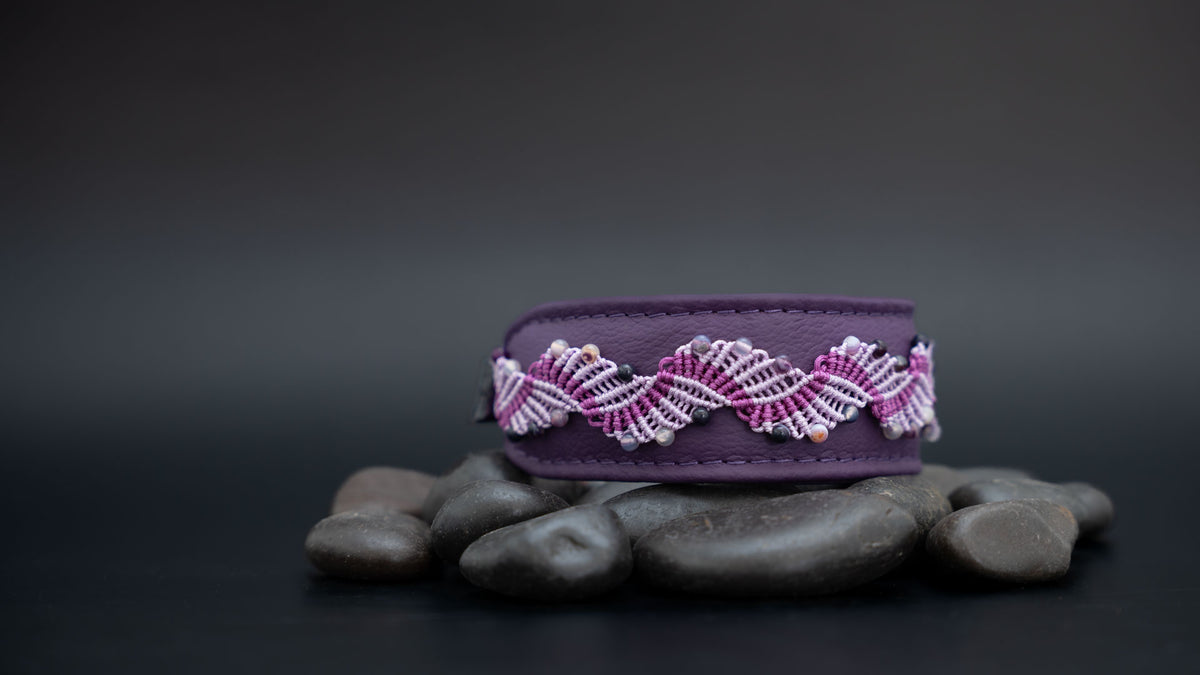 Violettes Makramee-Hundehalsband mit Amethyst-Perlen auf dunklen Steinen; links bleibt freier Raum im Querformat.