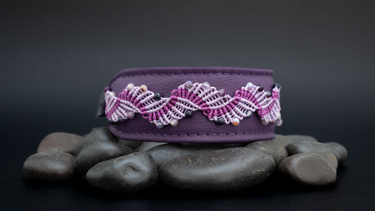 Violettes Amethyst-Hundehalsband mit zweifarbiger Makramee-Borte auf dunklen Steinen, leicht seitlich im Querformat