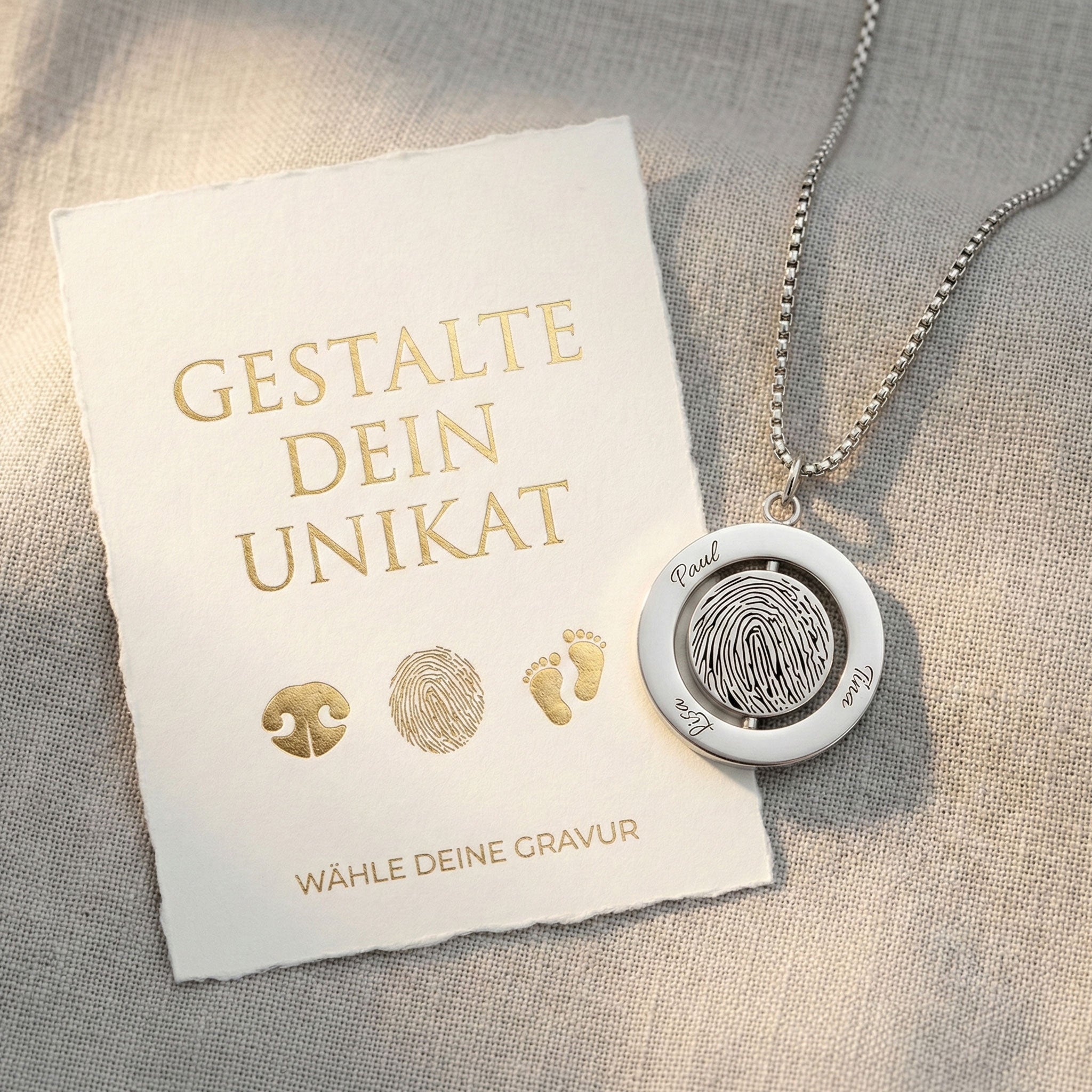 Silbernes Medaillon mit Fingerabdruck und Namensgravur neben einer Geschenkkarte