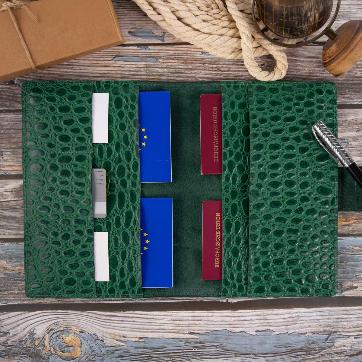Das geöffnete, befüllte Reise-Etui zeigt sein großzügiges Platzangebot. Eingebettet in weiches, grünes Nubuk-Hirschleder sind mehrere Reisepässe, EU-Heimtierausweise und Karten sicher verstaut.