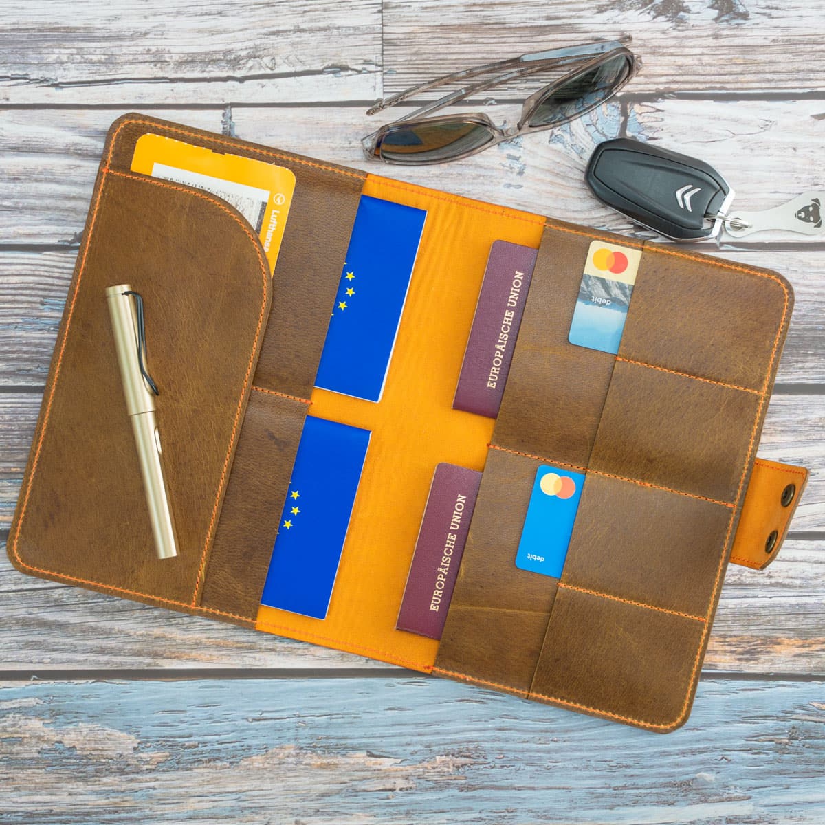 Befülltes Travel Wallet aus braunem Wasserbüffelleder mit orangem Innenfutter. Perfekt organisiert mit Reisepässen, Bankkarten und Reisedokumenten. Auch ideal als Hülle für den EU-Heimtierausweis.