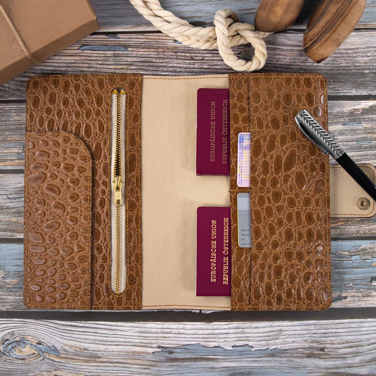 Das befüllte Travel Wallet zeigt seinen luxuriösen Innenraum aus Kroko geprägtem Rindsleder und hell-taupefarbenem Kalbsleder, sicher verstauten Reisepässen und einem robusten Reißverschlussfach mit einem Messing-Metall-Reißverschluss.