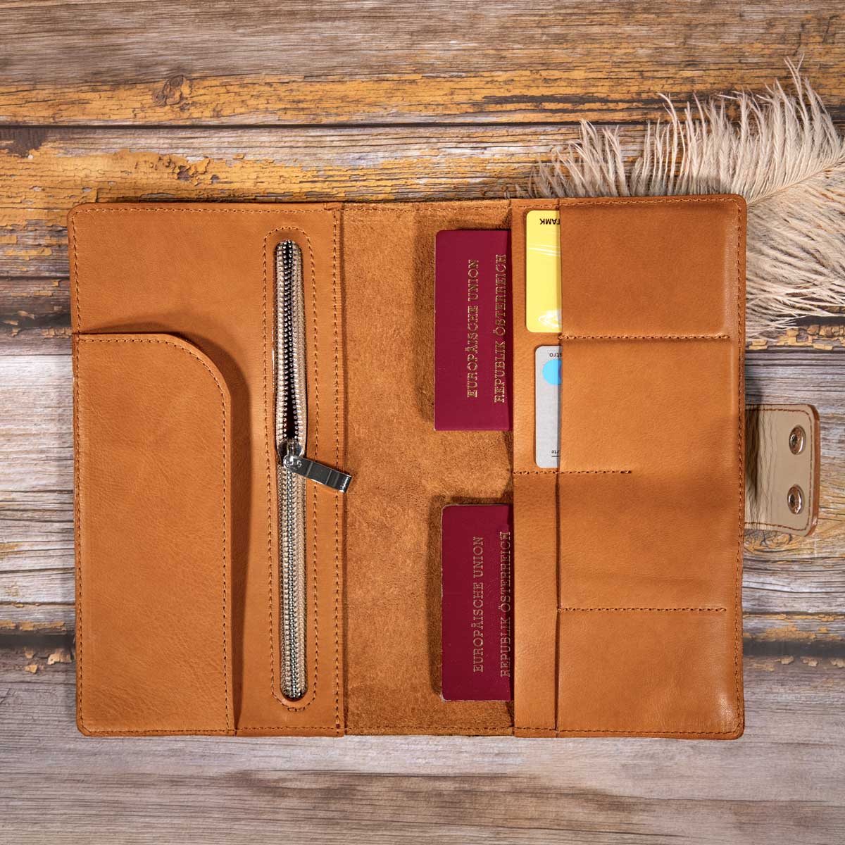 Travel Wallet aus cognacfarbenem Rindsnappa. Sichtbar sind Reisepässe, Kreditkarten und ein im großzügigen Reißverschlussfach verstautes Smartphone.