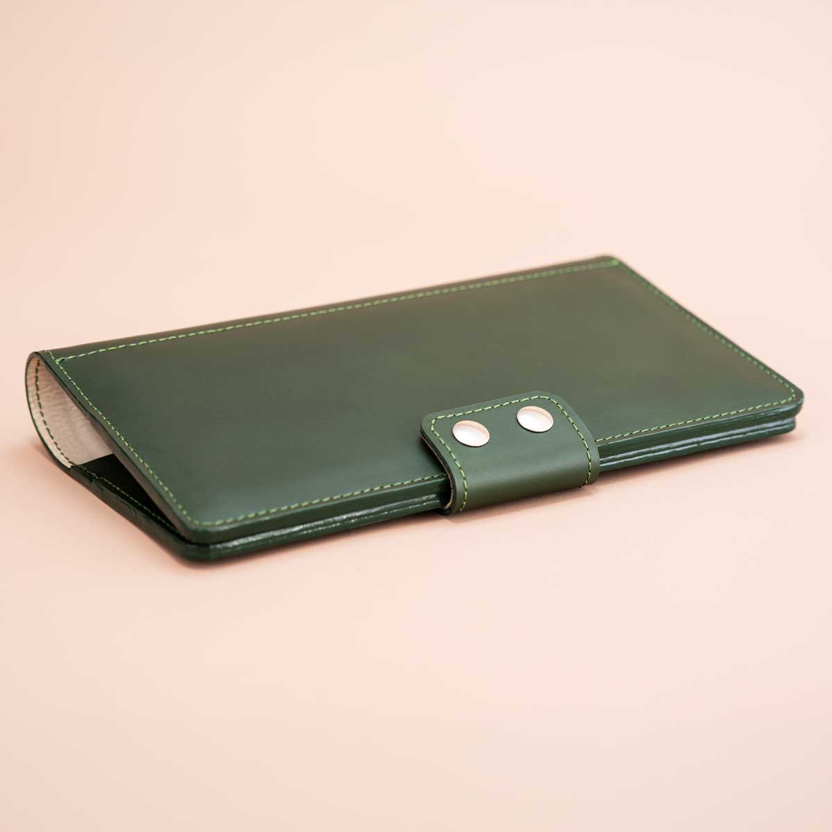 Flach liegendes, handgefertigtes Travel Wallet aus robustem, dunkelgrünem italienischem Taschenleder. Geschlossen wird das Reise-Etui mit zwei edlen silberfarbenen Druckknöpfen