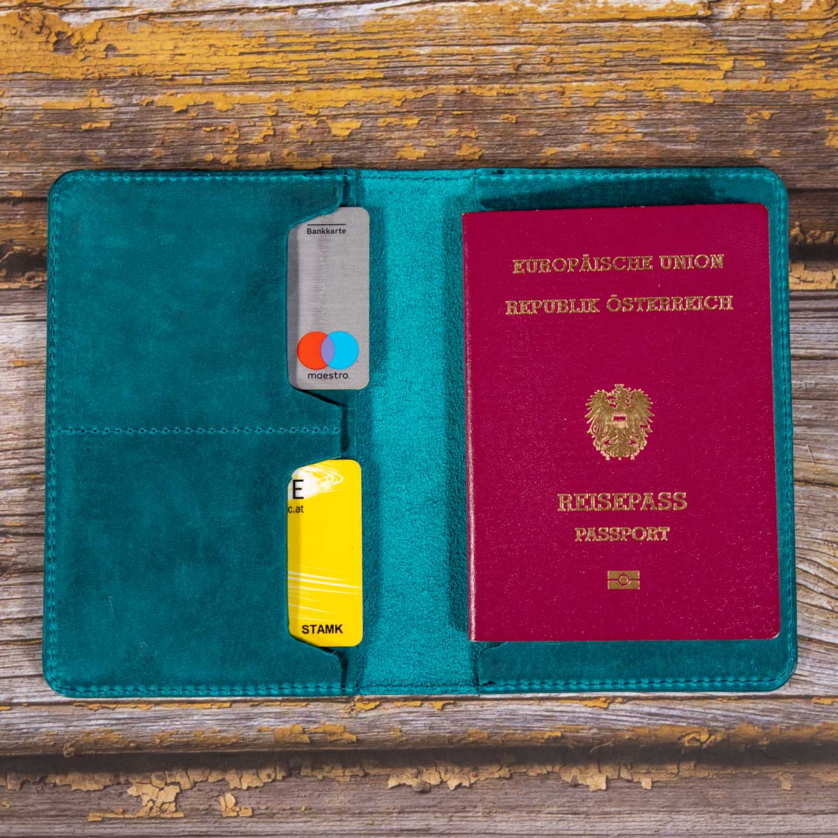 Geöffnete Reisepasshülle aus türkisfarbenem Leder mit eingestecktem österreichischen EU-Reisepass auf der rechten Seite.