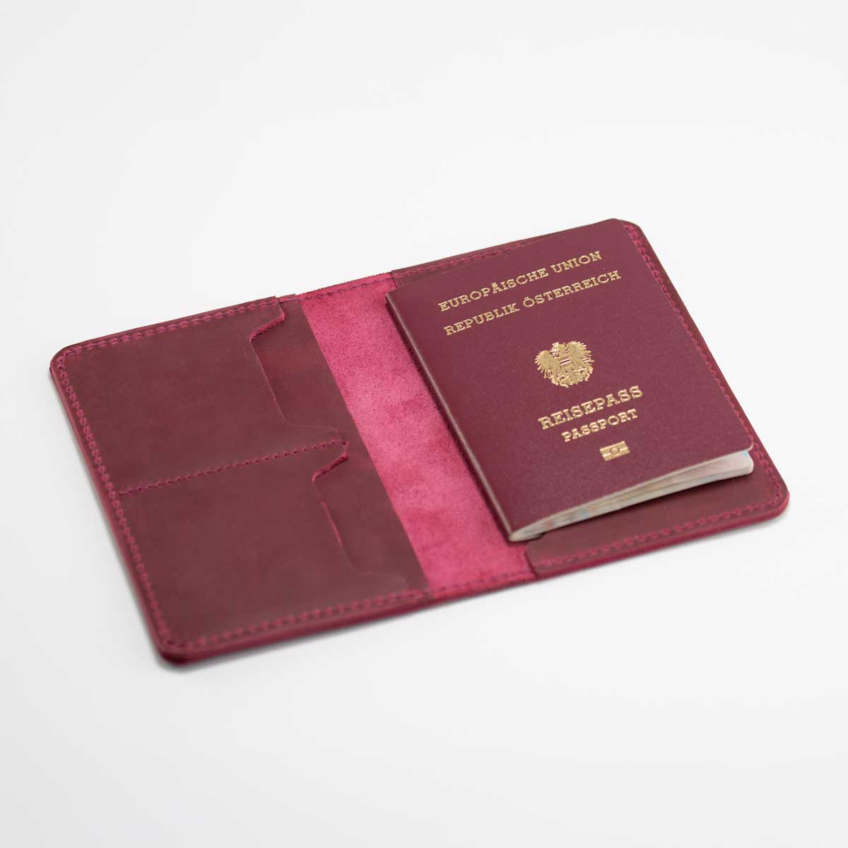 Geöffnete Reisepasshülle aus magentafarbenem Leder mit eingestecktem österreichischen EU-Reisepass auf der rechten Seite.