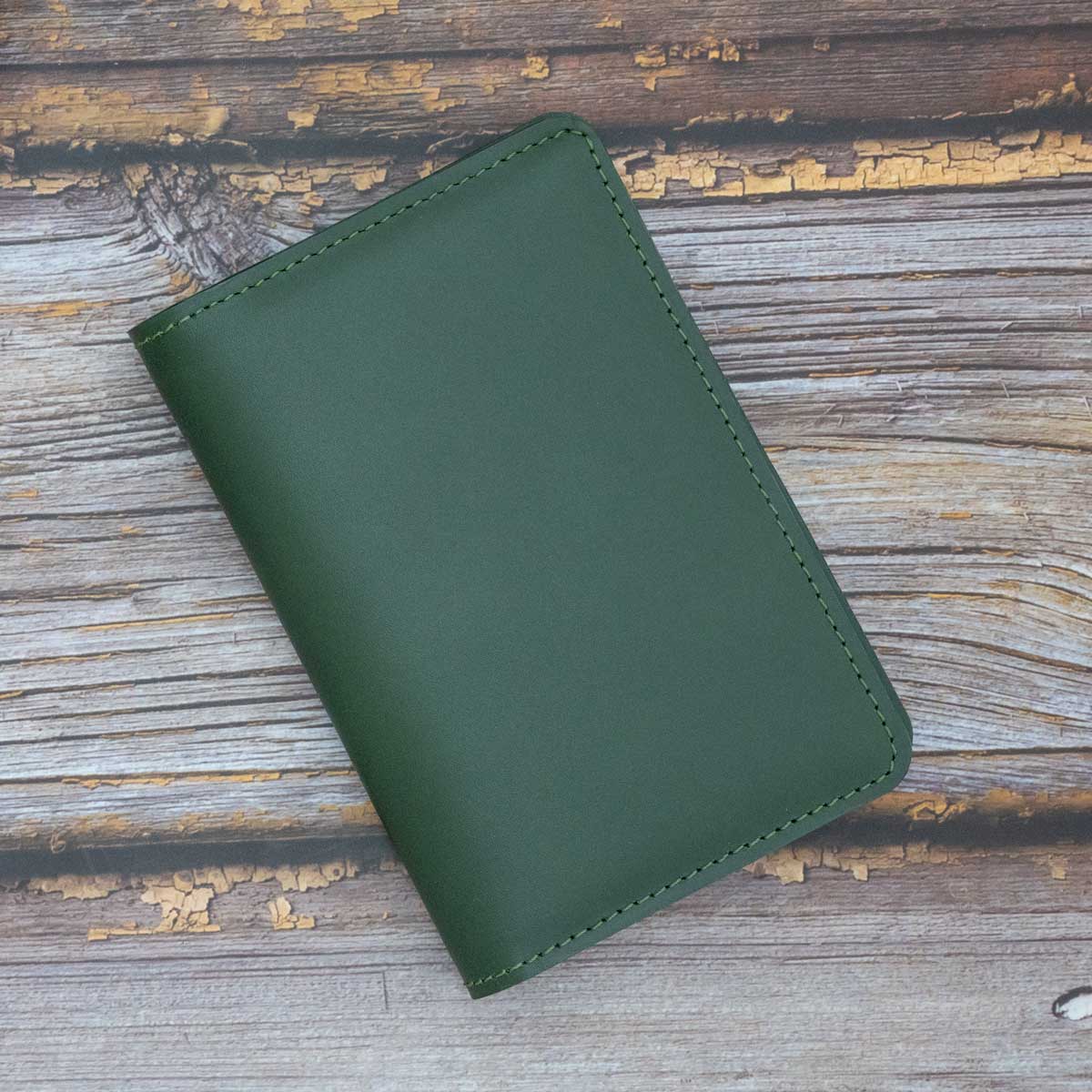 Vorderseite der geschlossenen, handgefertigten Leder-Reisepasshülle aus robustem, dunkelgrünem italienischem Taschenleder mit eleganten Ziernähten.
