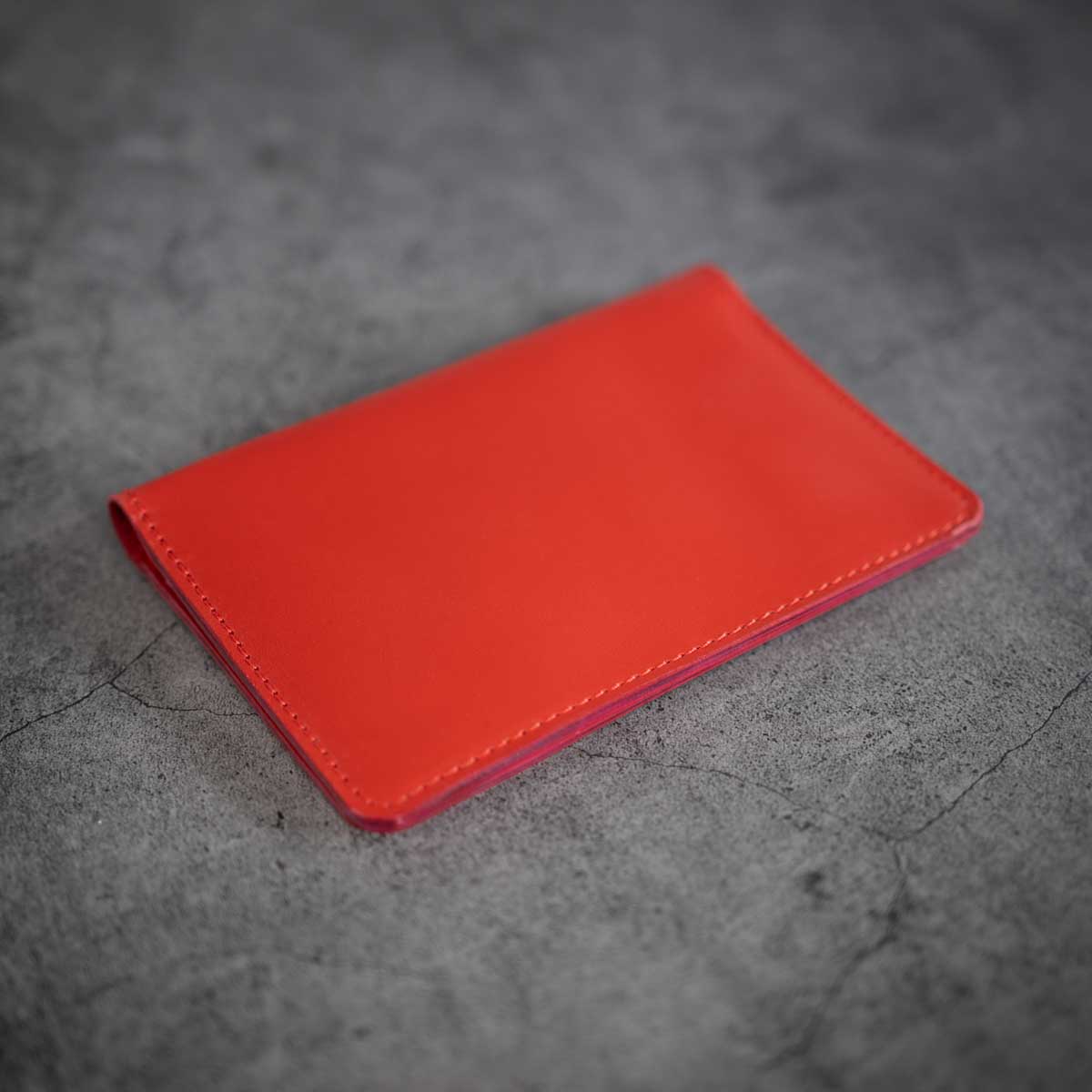 Vorderseite der geschlossenen, handgefertigten Leder-Reisepasshülle in leuchtendem Signalrot mit präziser, farblich abgestimmter Naht.