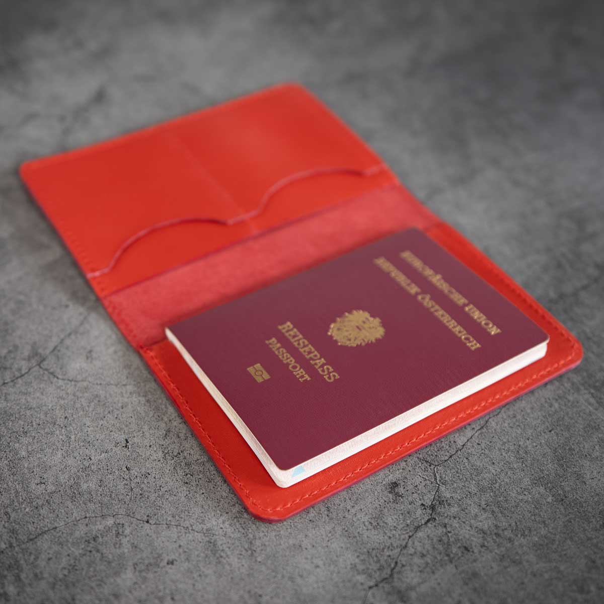 Geöffnete Reisepasshülle aus rotem Leder mit einem eingesteckten österreichischen Reisepass und Sicht auf die Kantenverarbeitung