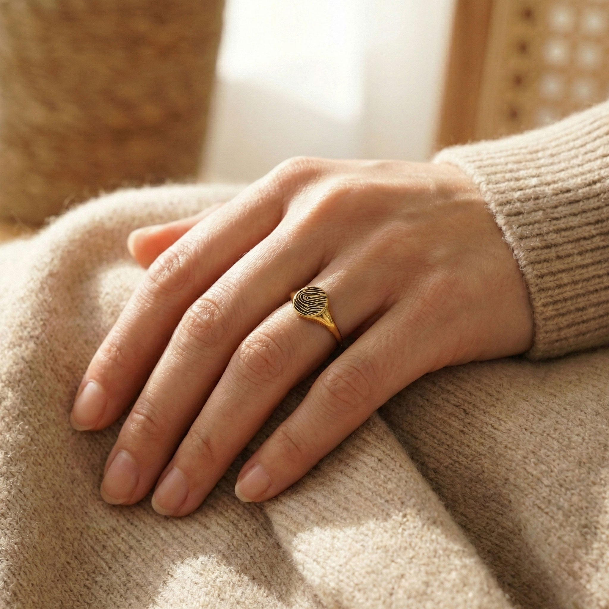 Frau trägt einen goldenen Siegelring mit Fingerabdruck-Gravur zur Strickjacke