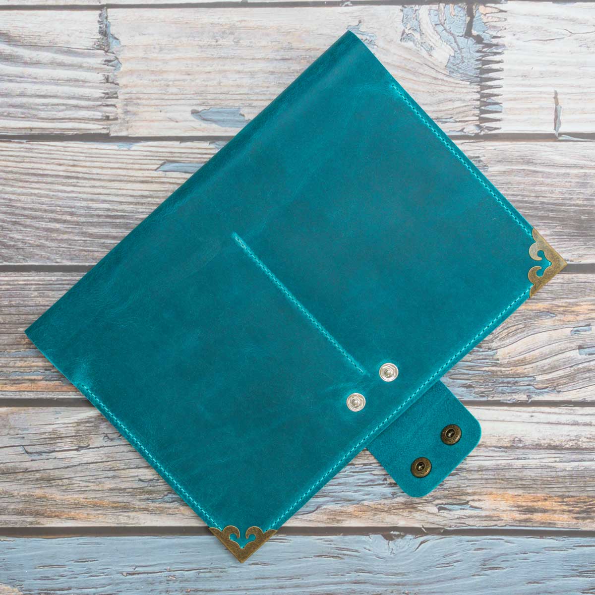 Geschlossenes Travel Wallet für vier Pässe aus türkisem Crazy Horse Leder. Die charakteristischen altmessingfarbenen Eckenschoner und Druckknöpfe unterstreichen den robusten Vintage-Look.