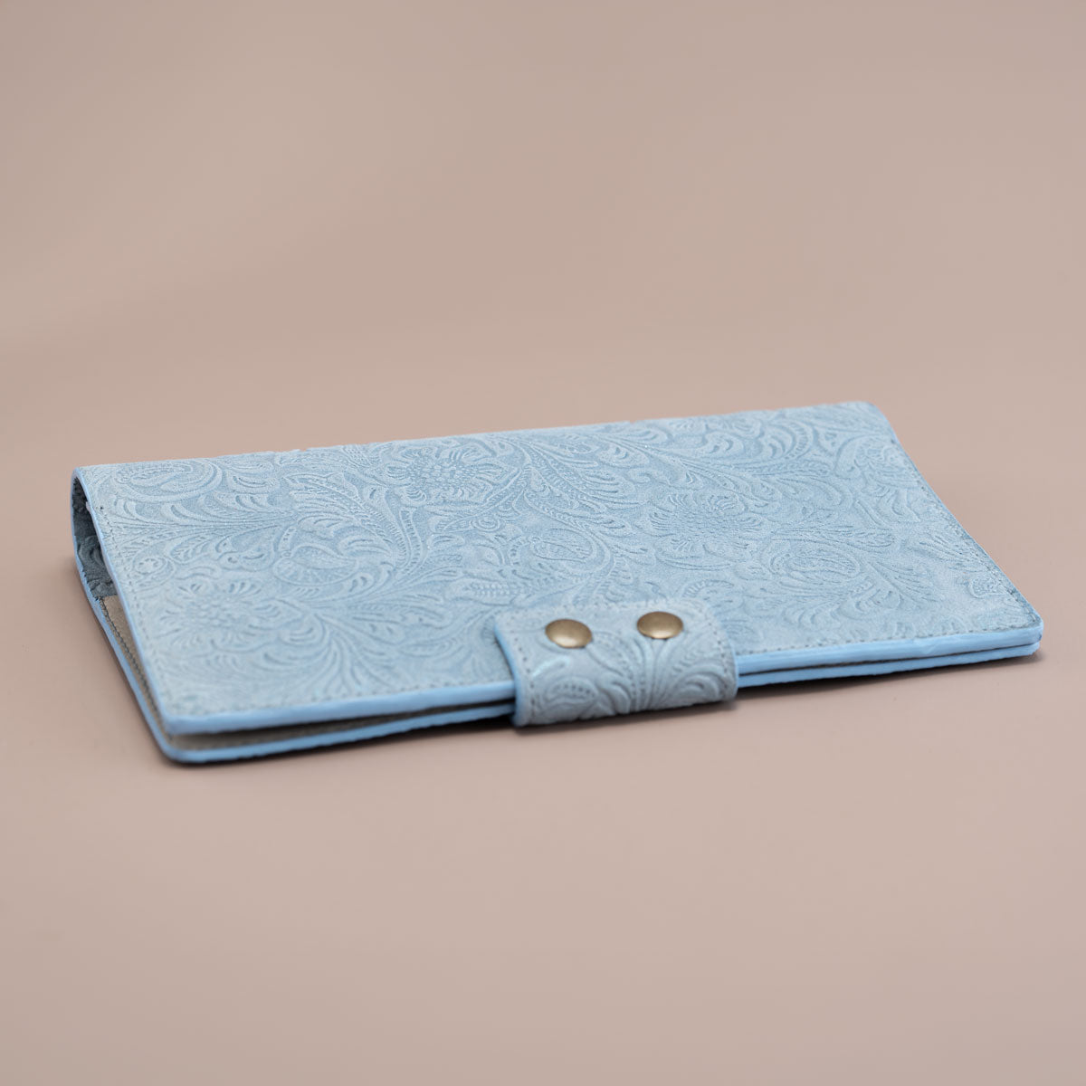 Flach liegendes Einzelstück-Travel Wallet aus hellblauem Leder mit Blumenprägung. Die handversiegelten Kanten betonen die hochwertige, österreichische Manufaktur-Qualität.