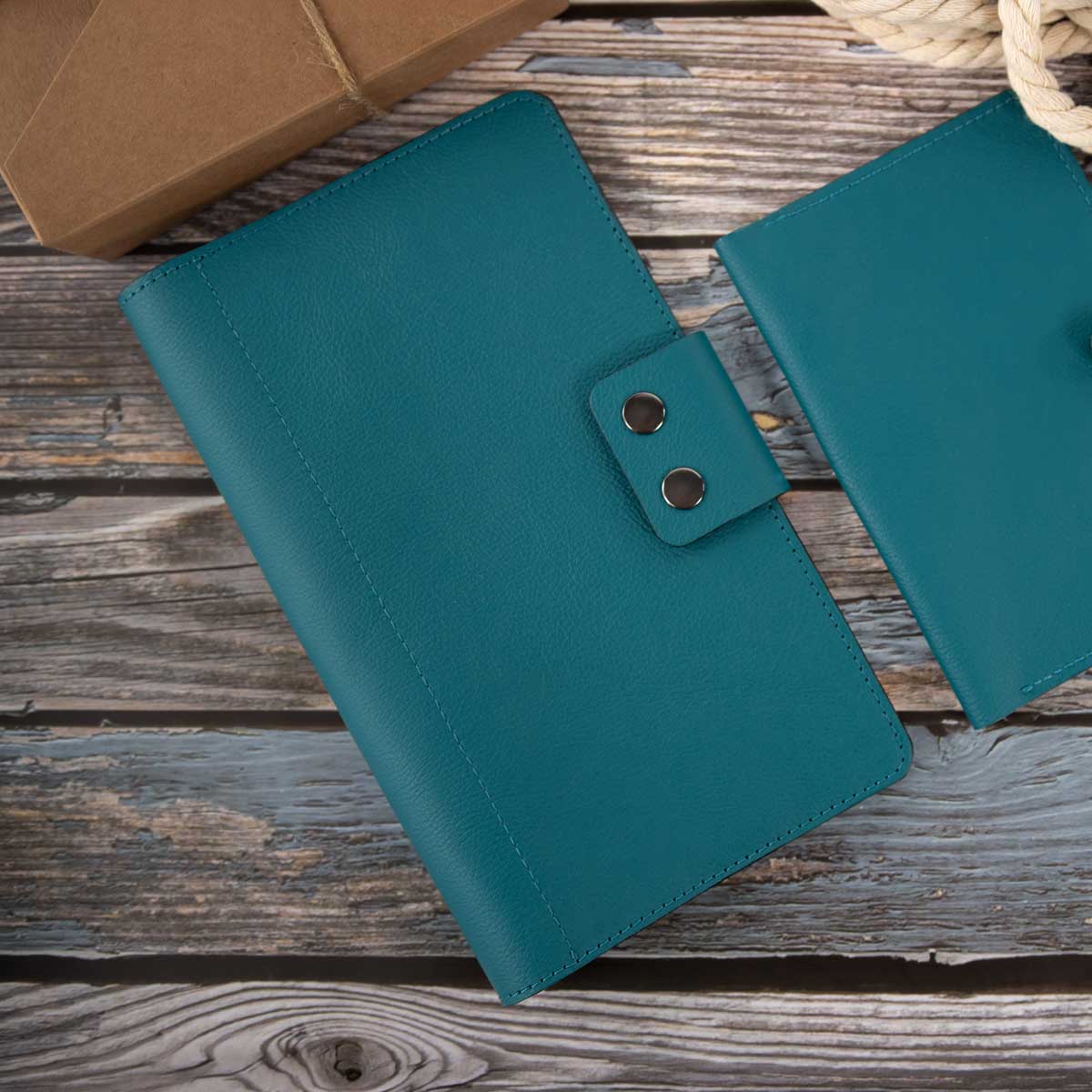 Elegantes petrolfarbenes Travel Wallet aus italienischem Taschenleder, liegend neben einem Paket auf einem Holztisch