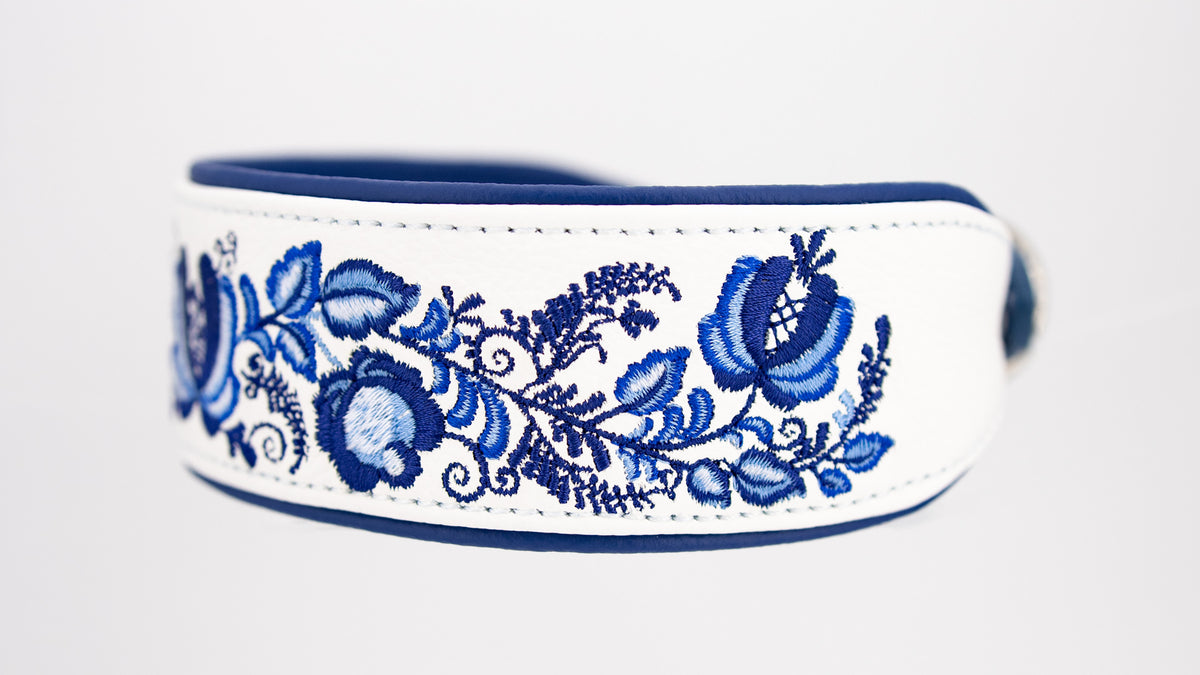 Detailaufnahme der floralen Gzhel-Ornamente mit blauen Blüten, geschwungenen Ranken und Blättern auf weißem Leder.