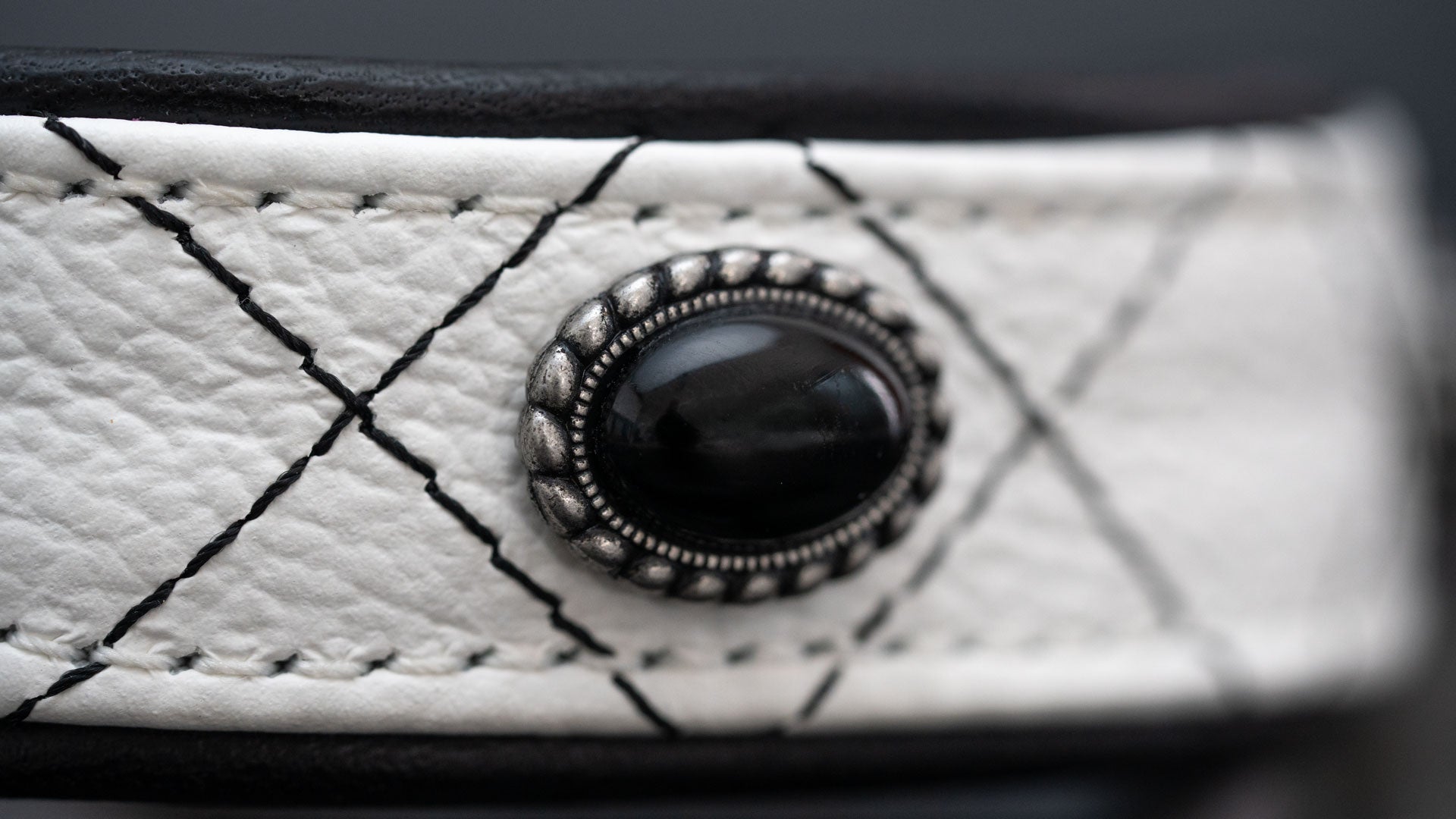 Detailansicht von schwarzem Onyx, Metallfassung und schwarzer Rhombensteppung auf weißem Leder