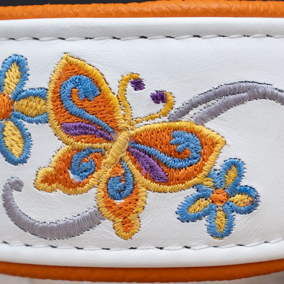 Detailansicht der bunten Schmetterlings-Stickerei auf weißem Nappaleder